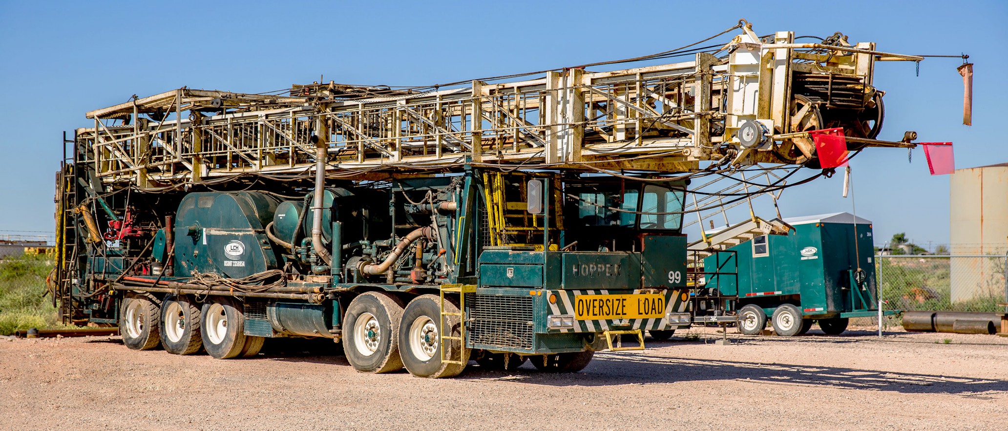 An industrial vehicle used for well servicing, featuring multiple metal frameworks, is labeled with 